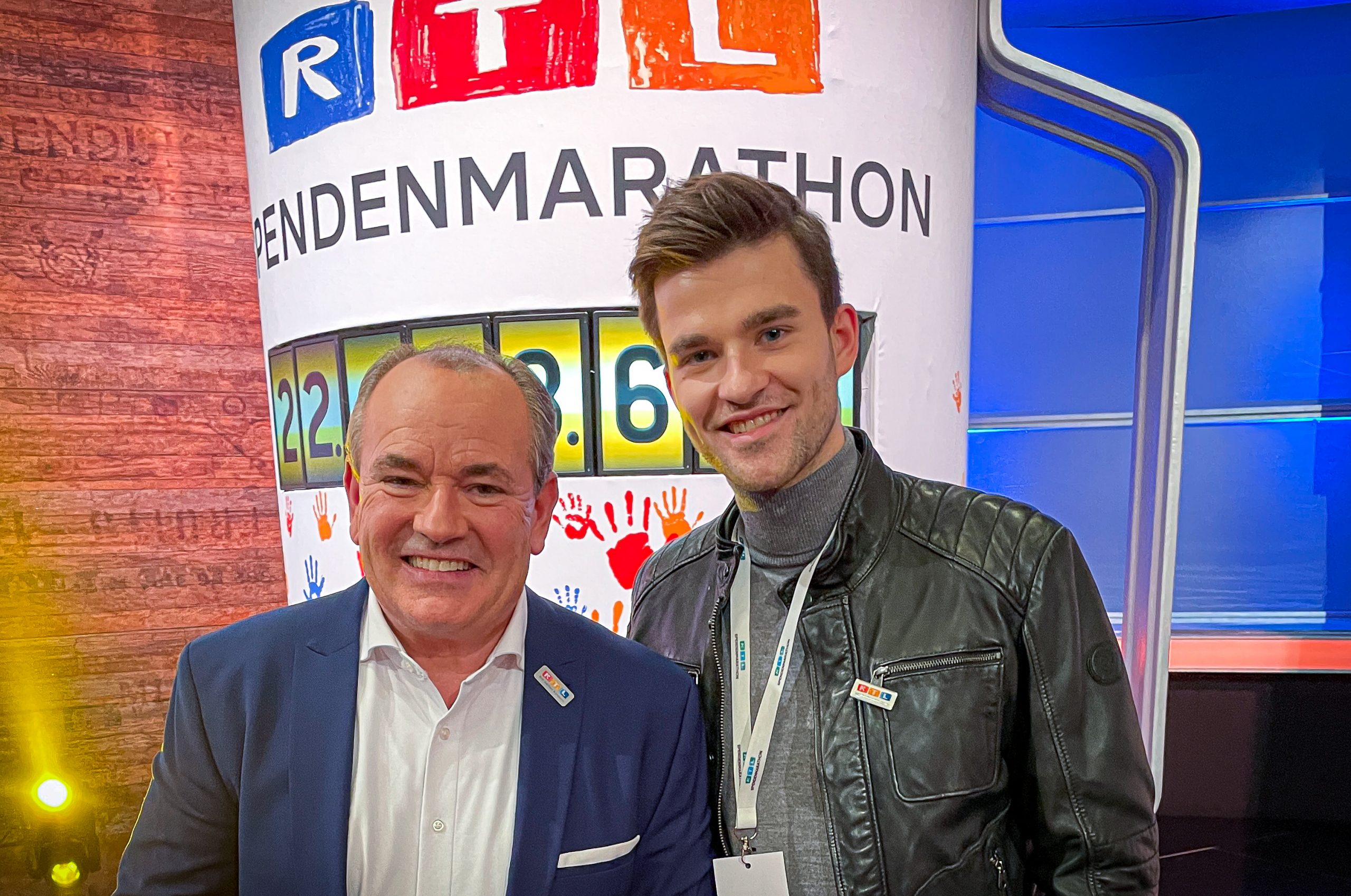 Moderator Wolfram Kons und Schauspieler Patrick Mölleken stehen vor der Spendenuhr des 21. RTL-Spendenmarathons 2021.